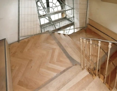 Escalier intérieur en bois clair avec rampe à balustres tournés, palier d'étage avec parquet à chevrons