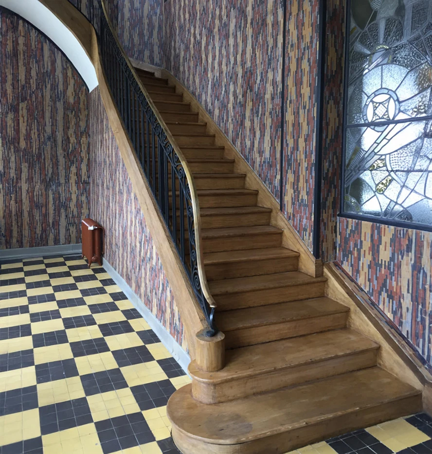 Escalier intérieur en bois clair avec rampe à balustres tournés, palier d'étage avec parquet à chevrons